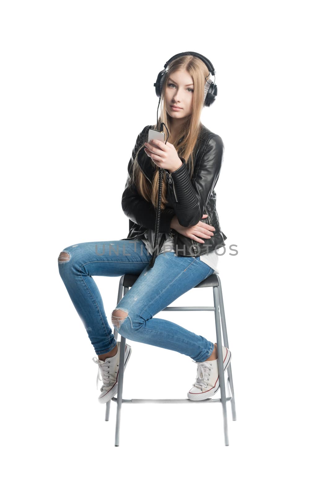 The isolated on white portrait of a serious teenager girl in wired headphones listening music from personal phone