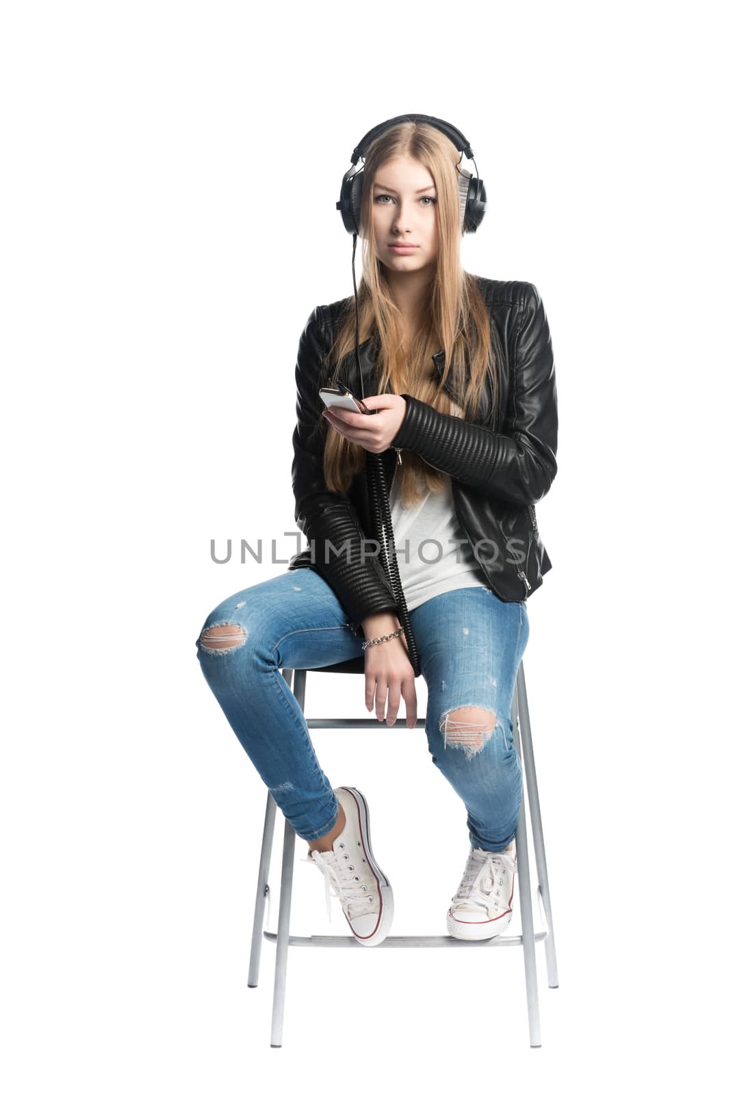 The isolated on white portrait of a serious teenager girl in wired headphones listening music from personal phone