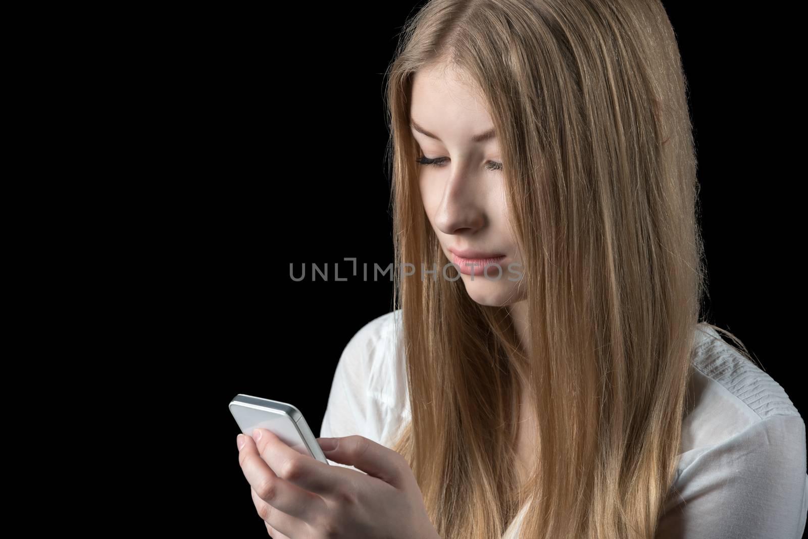 Attractive young girl feels depressed after reading bad news on her mobile cellular phone. Isolated on black.