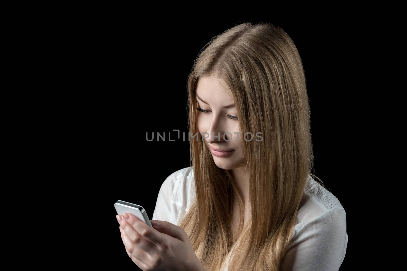 Young pretty girl enjoying social network on her personal cellular mobile phone. Isolated on black.