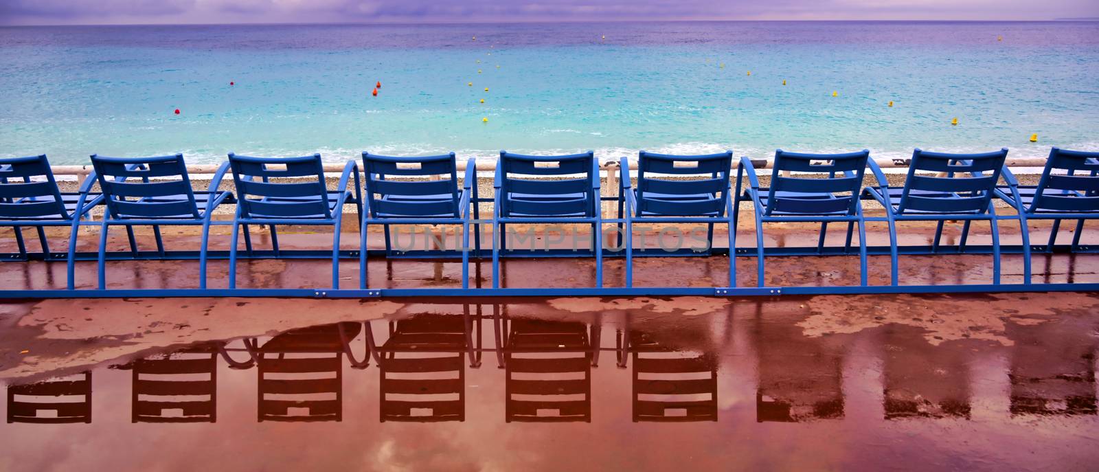 Blue chairs along the Promenade des Anglais on the Mediterranean Sea at Nice, France along the French Riviera.