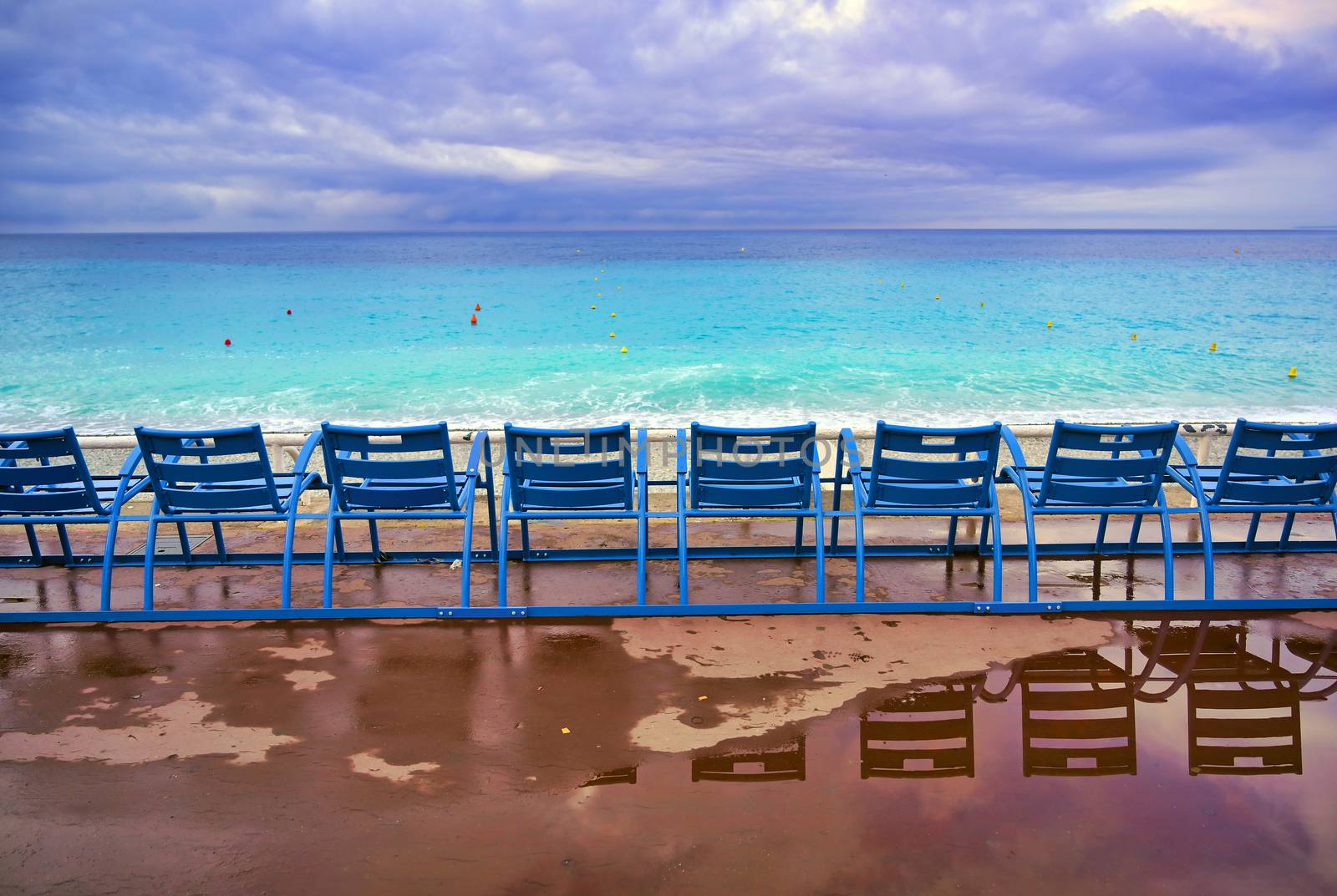 Blue chairs along the Promenade des Anglais on the Mediterranean Sea at Nice, France along the French Riviera.