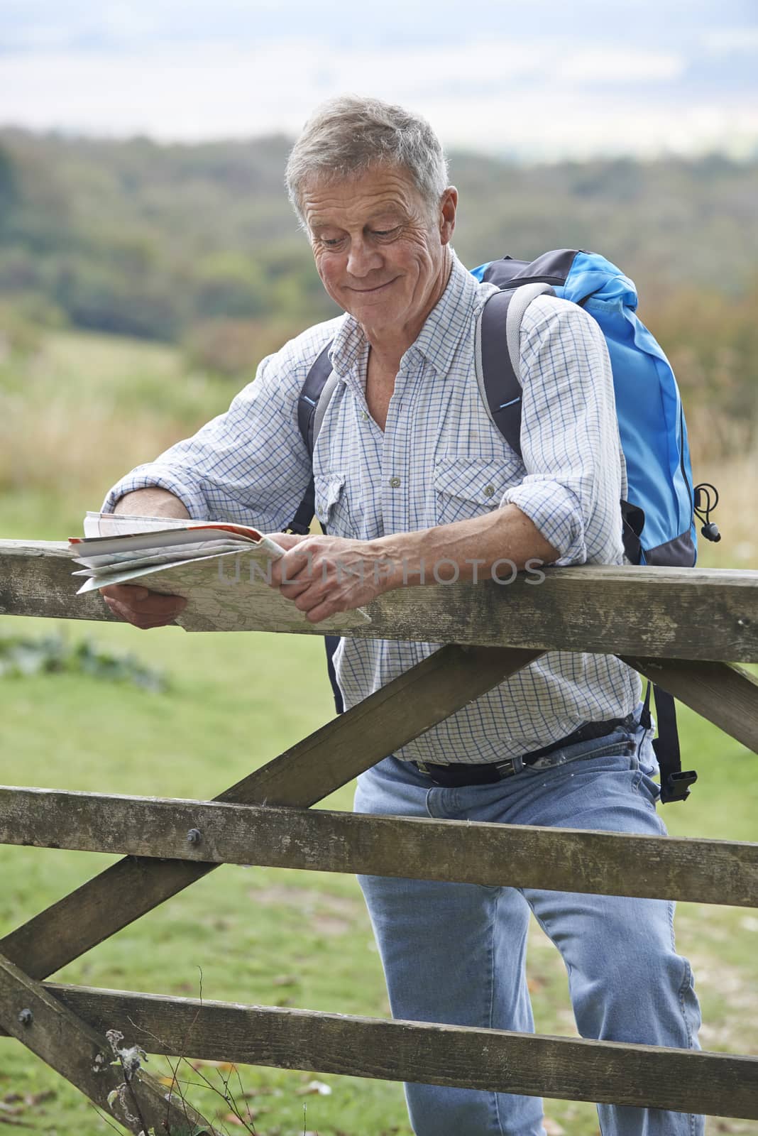 Senior Man Hiking In Countryside Resting By Gate