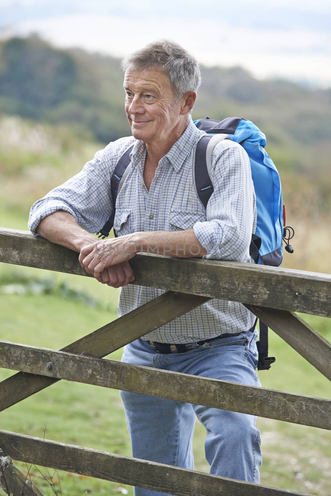 Senior Man Hiking In Countryside Resting By Gate