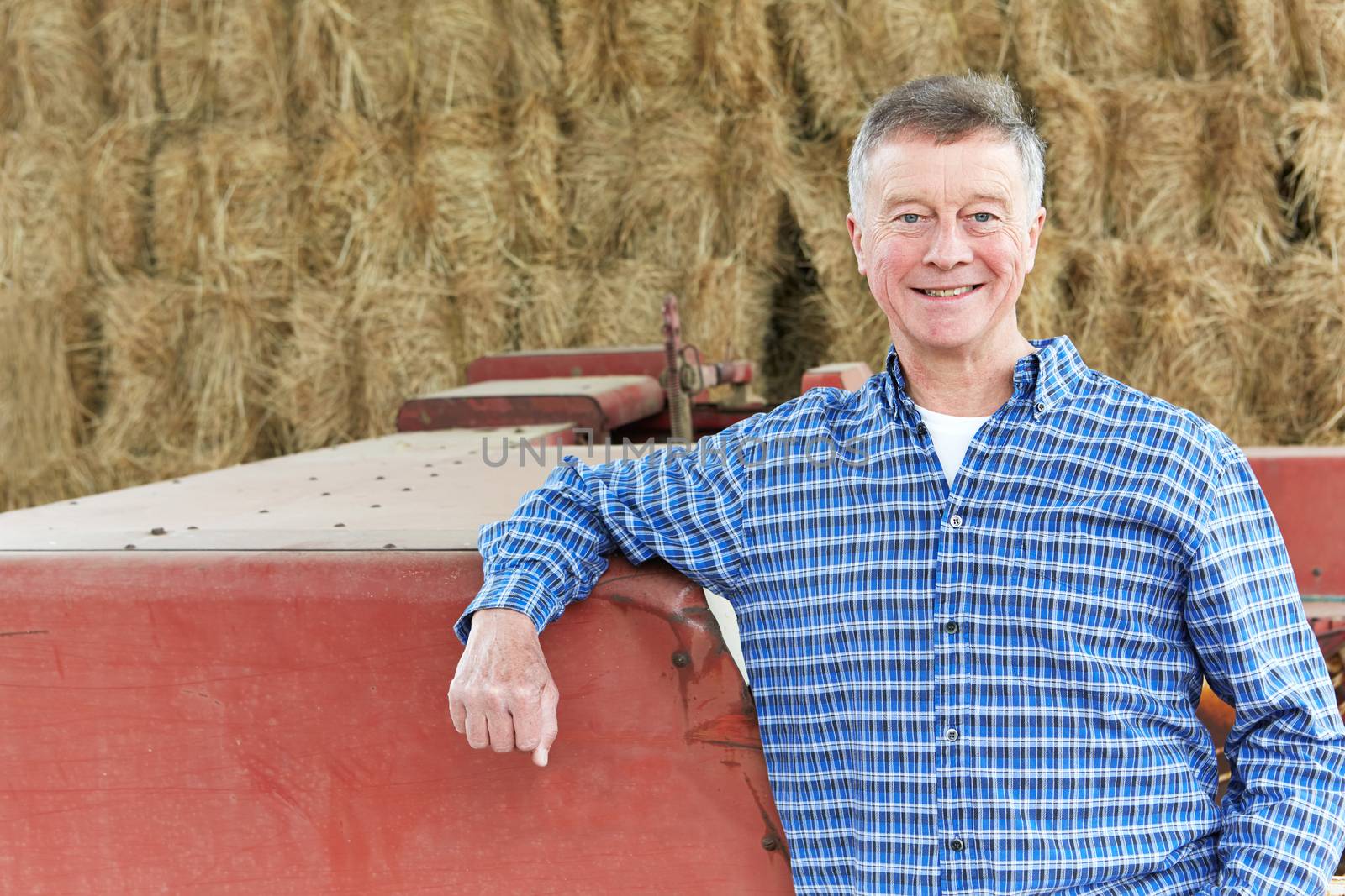 Farmer Standing Next To Farm Machinery In Barn