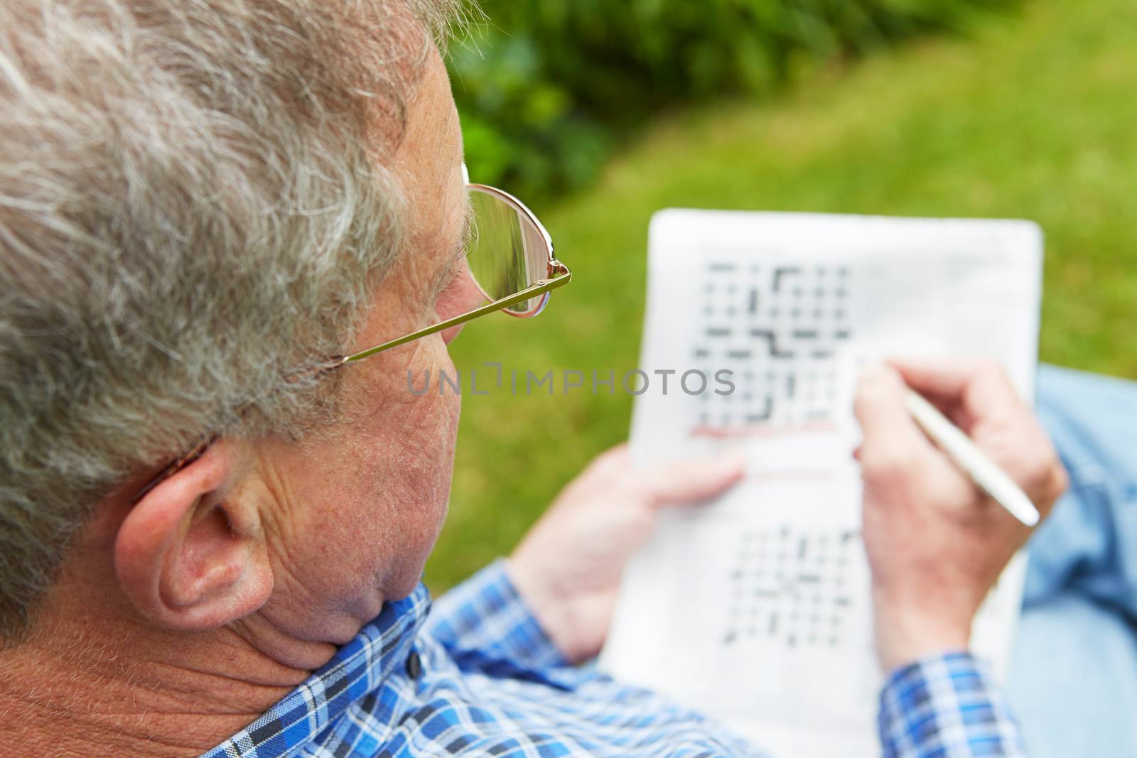 Senior Man Doing Crossword Puzzle In Garden