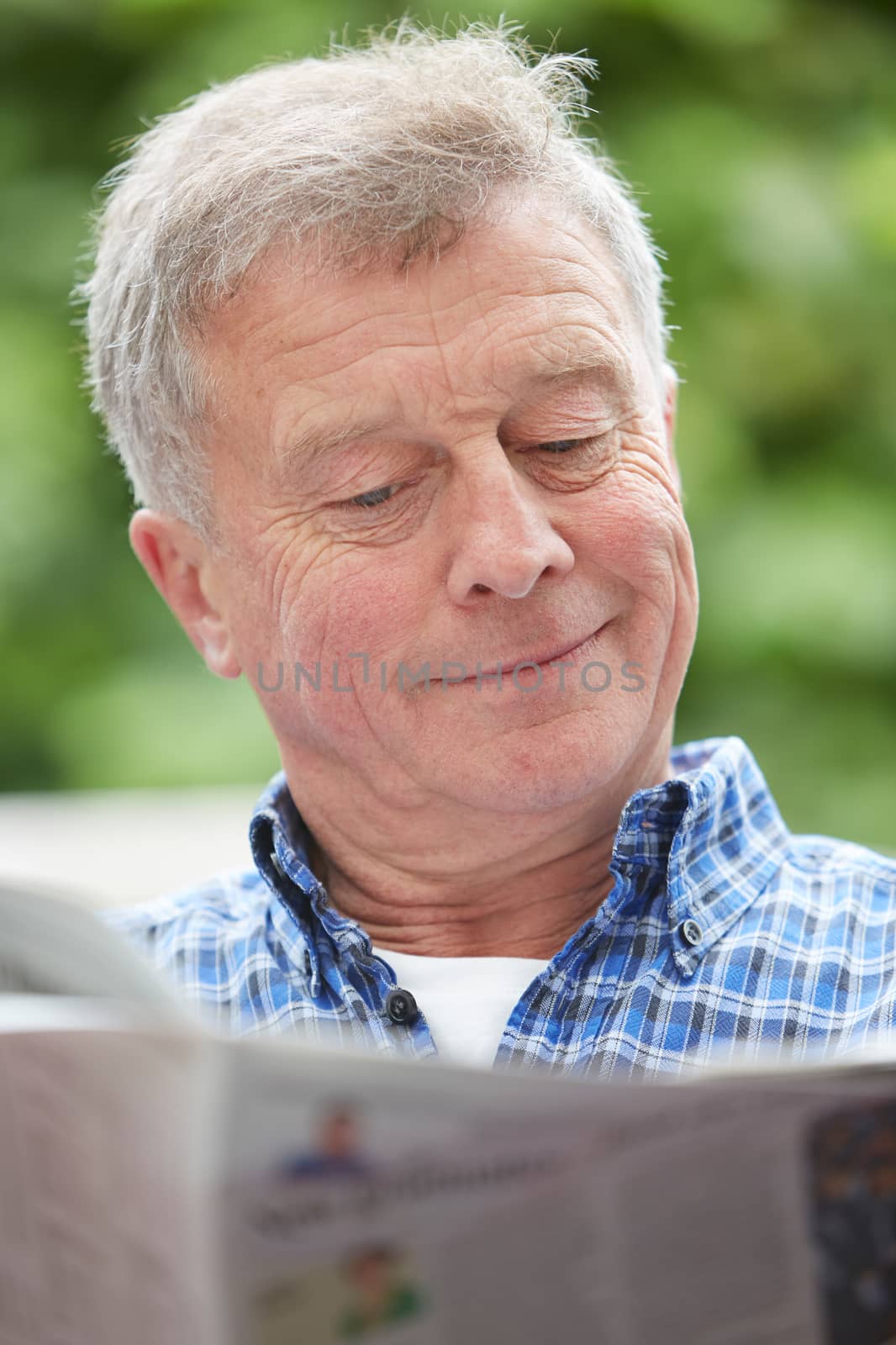 Senior Man Reading Newspaper Outdoors At Home