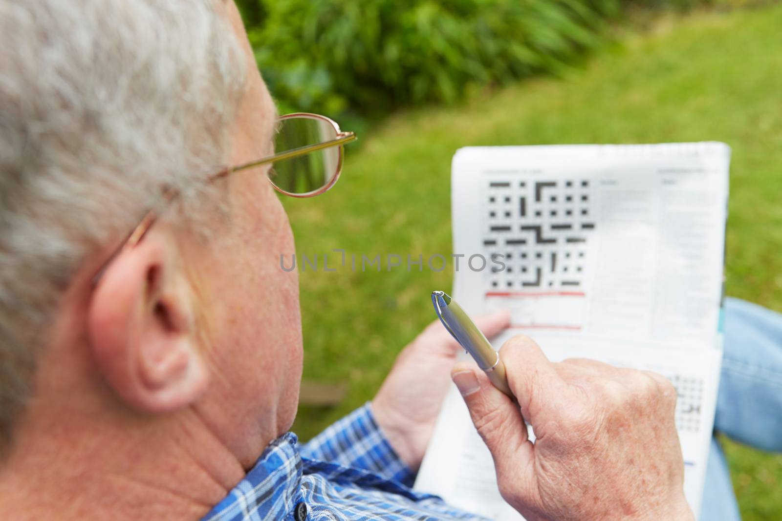 Senior Man Doing Crossword Puzzle In Garden by HWS