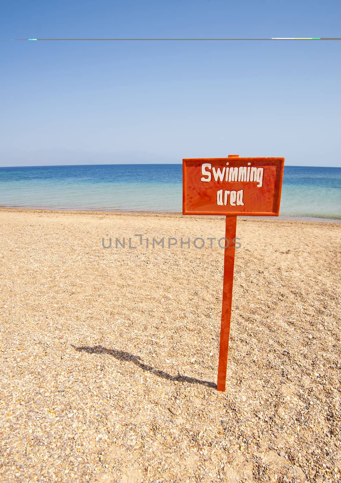 View out to sea from a tropical beach with a swimming area sign