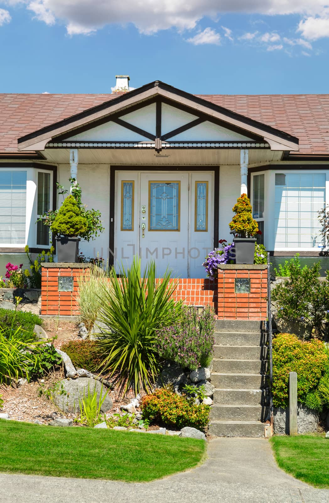 Entrance of a house with nicely landscaped front yard on blue sky background