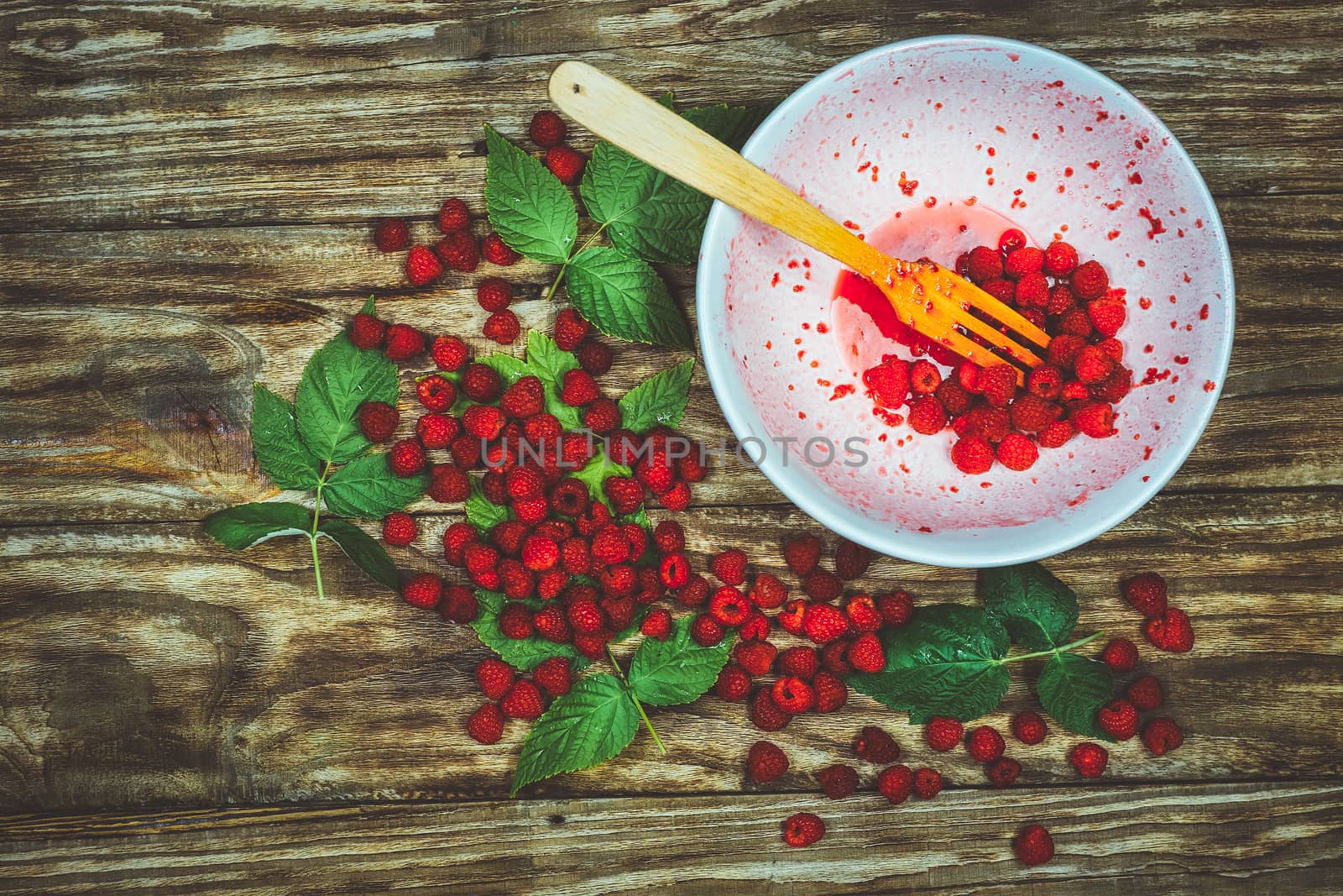 Ripe sweet raspberries in bowl, wooden fork on wooden table. Close up, top view. Red fresh raspberries on brown rustic wood background. flat lay with copy space.