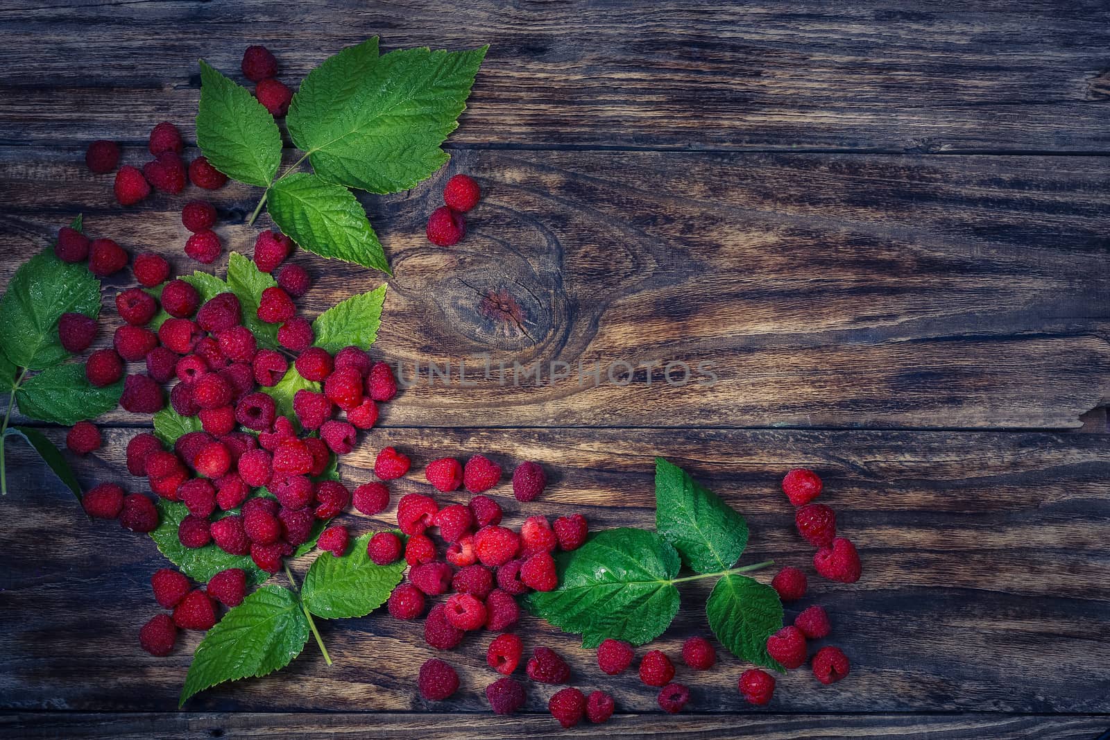 Fresh organic fruit - raspberry on wood background selective focus. Natural ripe organic berries with peduncles, green leaves, top view, flat lay with copy space.