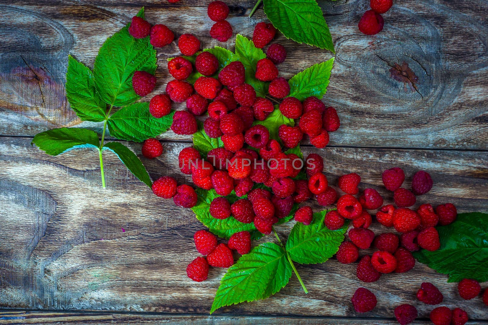 Fresh organic fruit - raspberry on wood background selective focus. Natural ripe organic berries with peduncles, green leaves, top view, flat lay with copy space.
