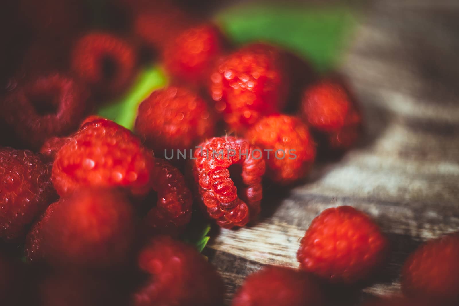 Fresh organic fruit - raspberry on wood background selective focus. Natural ripe organic berries with peduncles, green leaves, top view, flat lay with copy space. Bokeh.