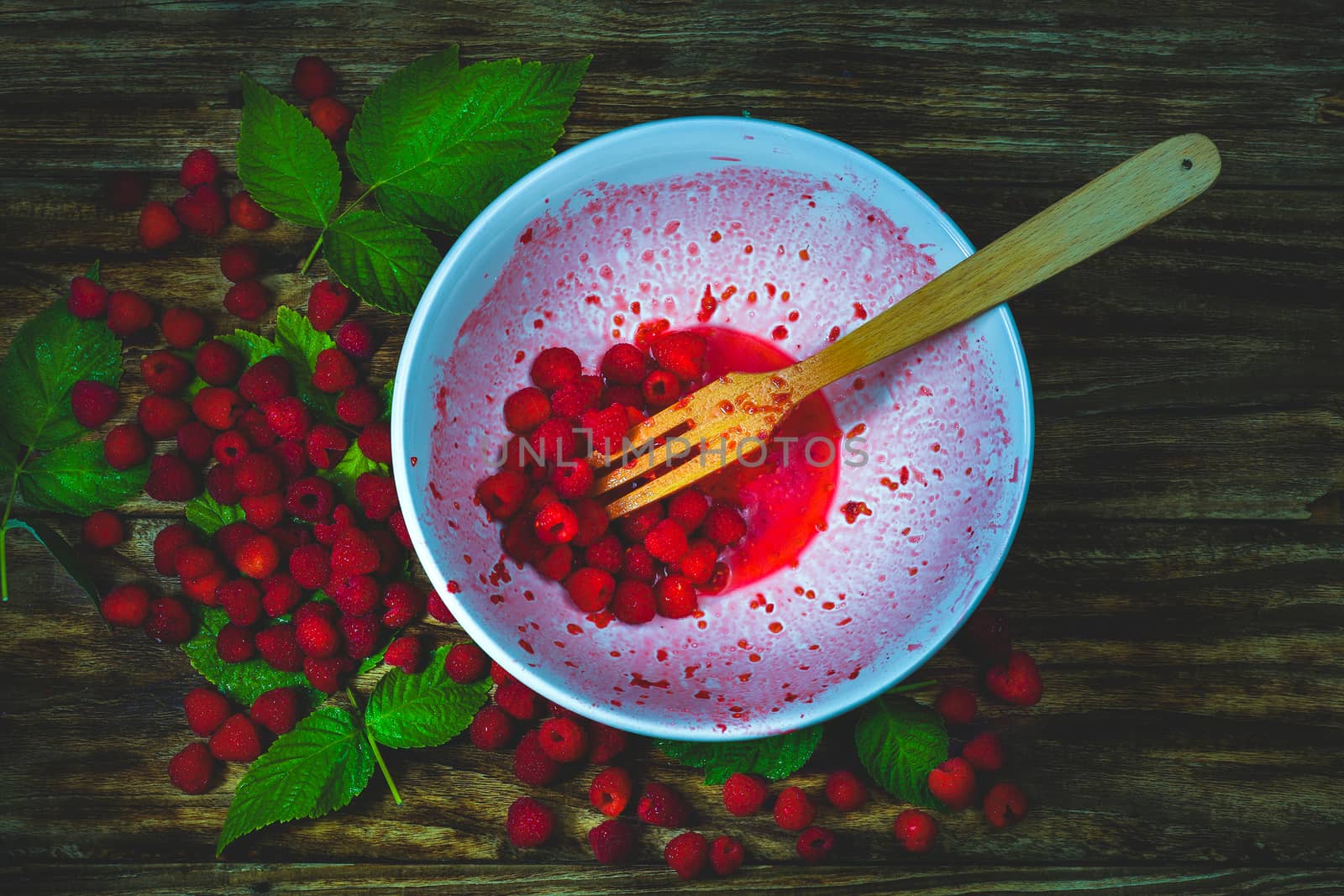 Ripe sweet raspberries in bowl, wooden fork on wooden table. Close up, top view. Red fresh raspberries on brown rustic wood background. flat lay with copy space.
