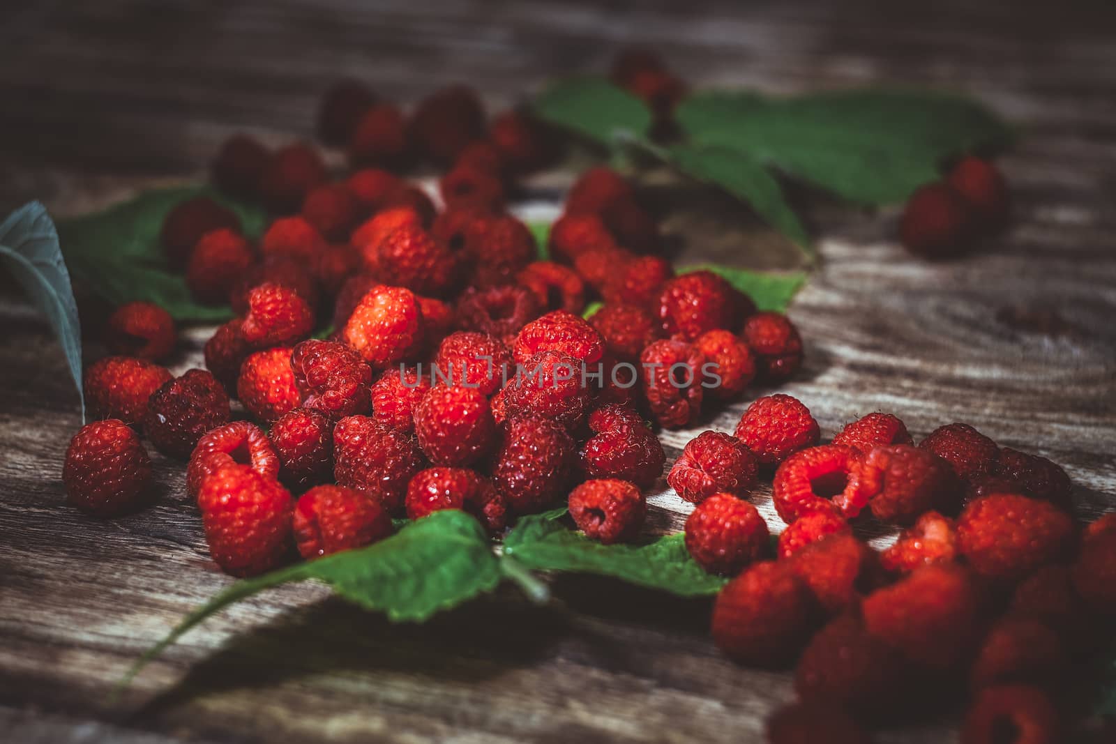 Fresh organic fruit - raspberry on wood background selective focus. Natural ripe organic berries with peduncles, green leaves, top view, flat lay with copy space.