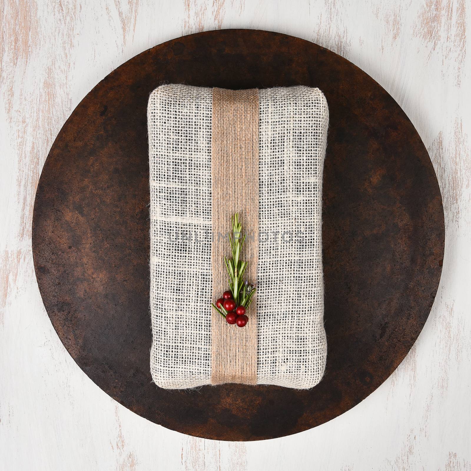 Fabric wrapped Christmas gift on a dark round stone surface on top of a rustic wood table. Square format from a high angle.