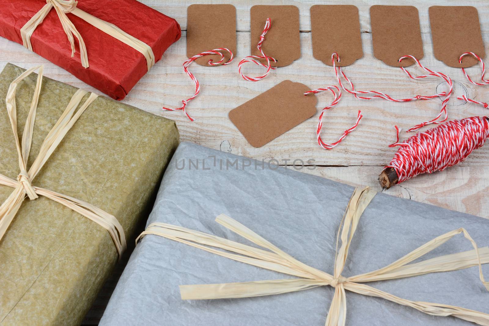 Overhead shot of a group of blank gift tags surrounded by wrapped Christmas presents on a white rustic table. Horizontal format with focus on the gift tags.