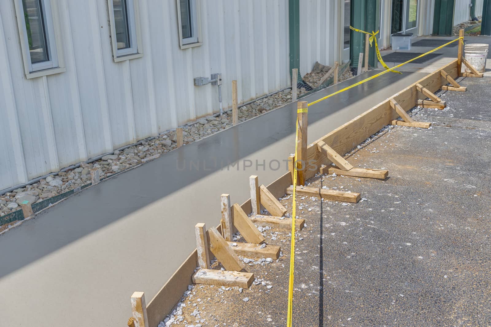 Horizontal shot of a freshly poured concrete sidewalk with caution tape in front of it.