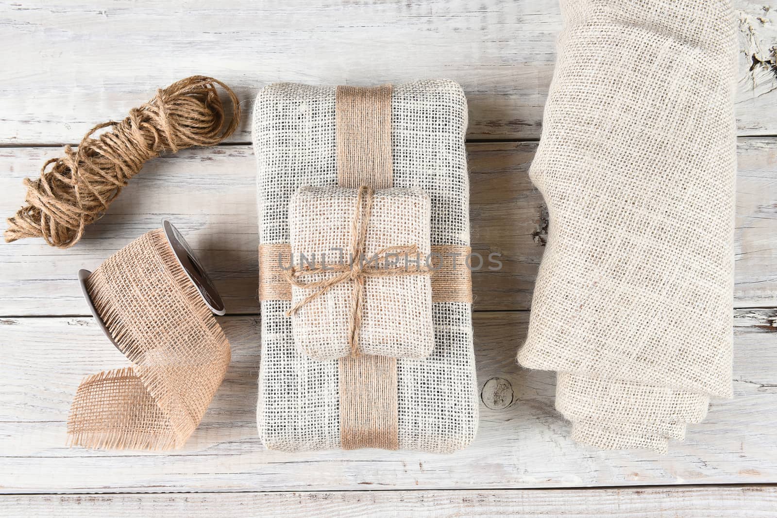 Top view of the tools for wrapping Christmas presents with burlap fabric and ribbon with twine on a white wood surface.