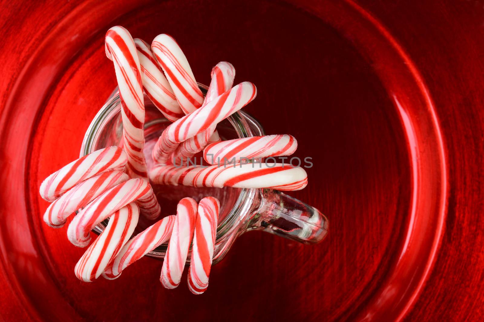 High angle shot of a group of Christmas candy canes in a mason jar on a red plate.