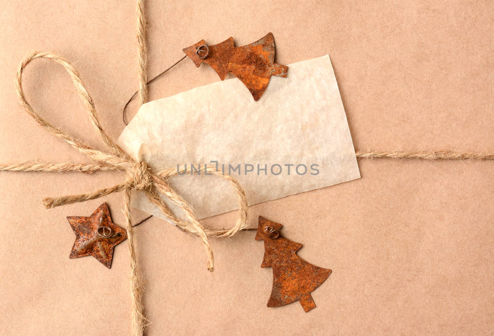 Closeup of a gift tag on a Christmas present. The package is wrapped in plain brown paper with a tied with twine. The package is adorned with metal star and christmas tree ornaments. Horizontal Format.