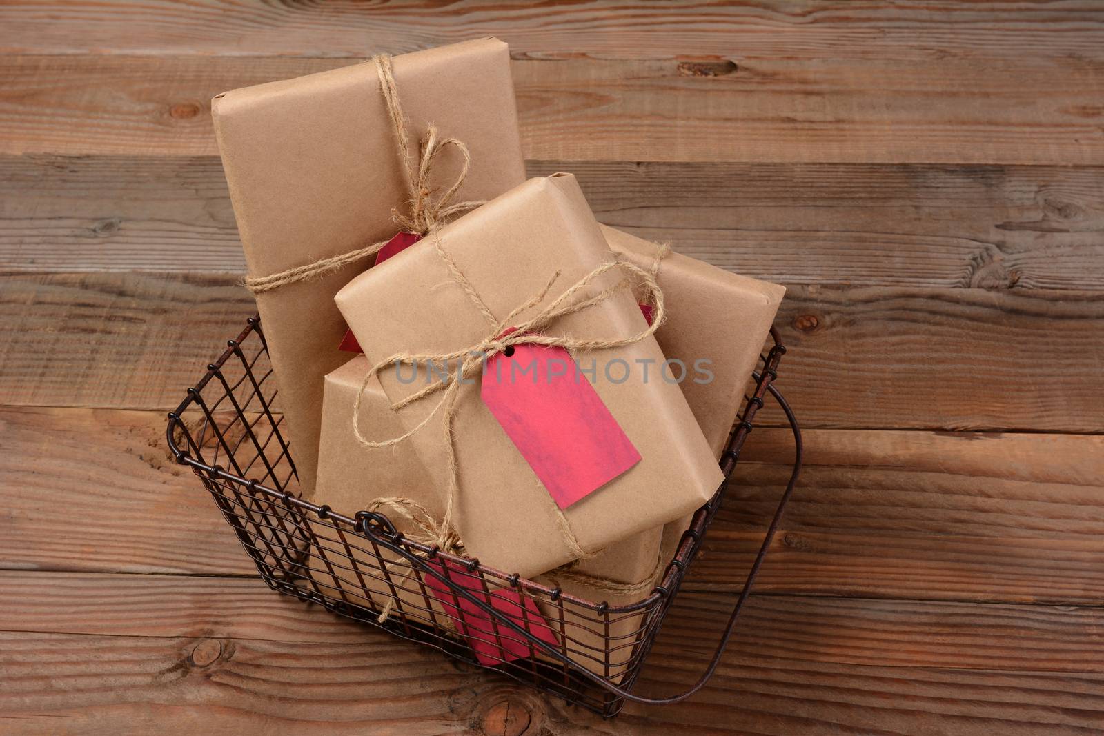 High angle shot of Christmas Presents wrapped in eco friendly craft paper ina a wire shopping basket. Horizontal format on a rustic wooden table.