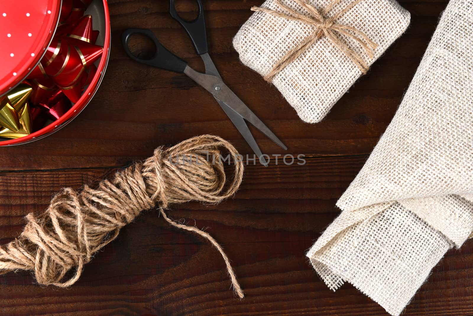 Fabric wrapped present with a tin of ribbon and bows. Top view on a rustic dark wood table. 