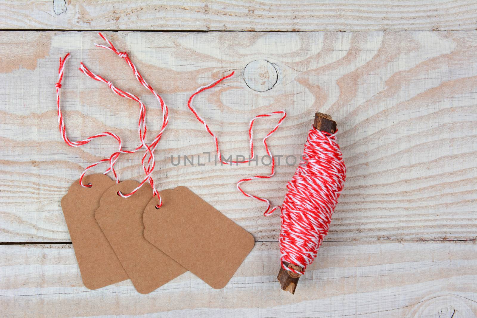 High angle view of blank Christmas Gift tags next to a spool of string on a whitewashed rustic wood table. The tags are blank and the string is wound around a twig.