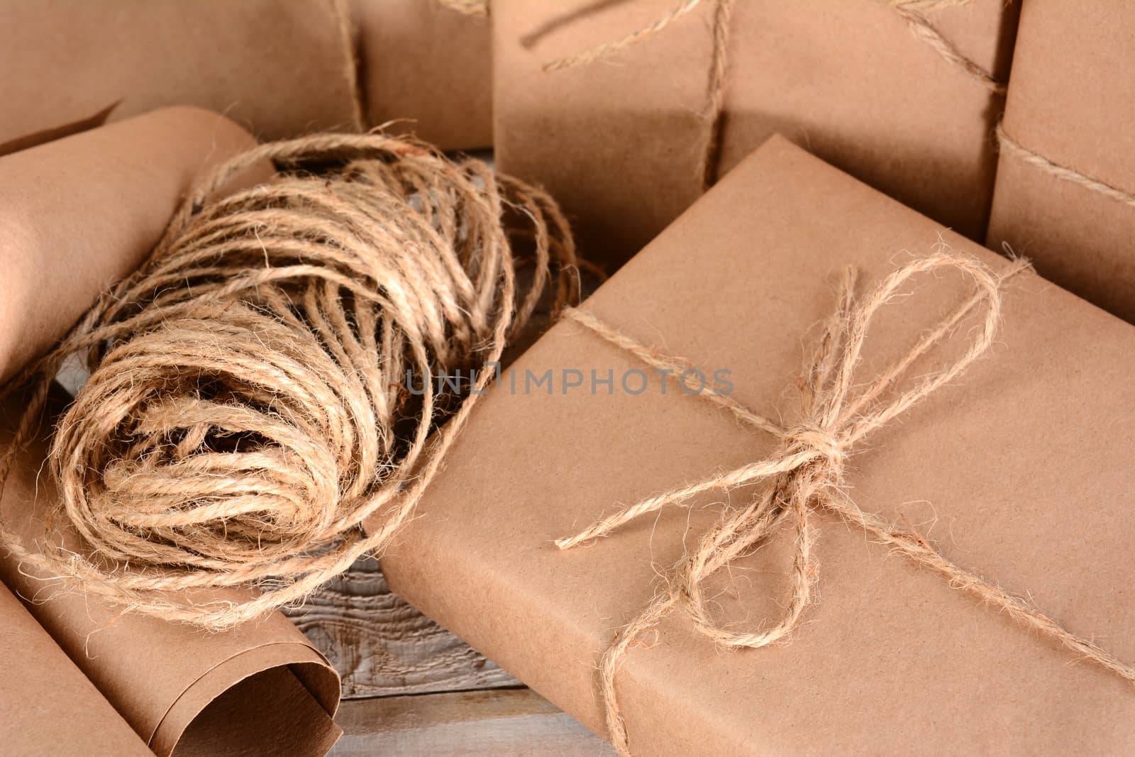 Closeup of a group of packages wrapped with plain brown paper and twine. Horizontal format on a wood table.
