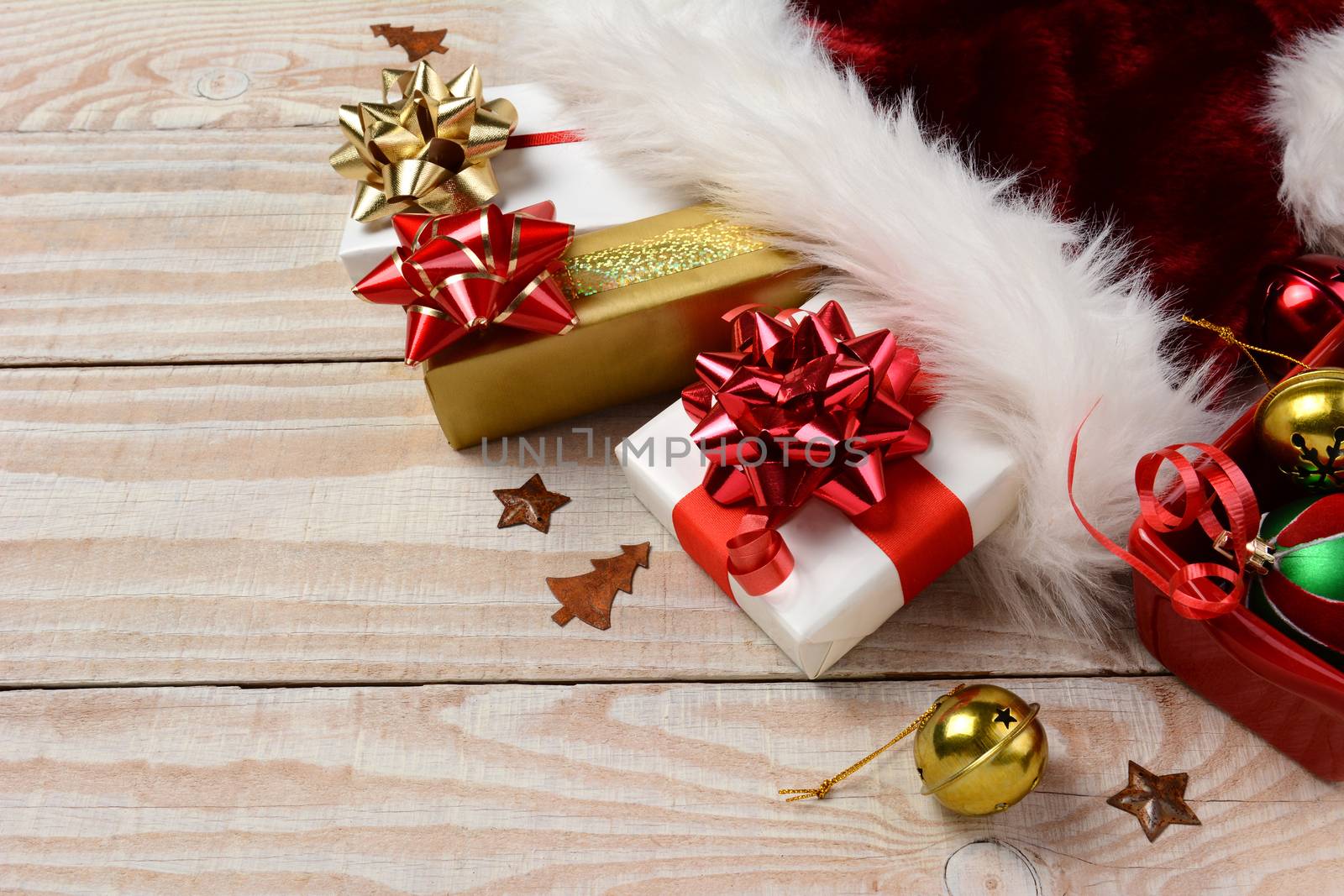 High angle closeup of Christmas presents and Santa Claus hat on a rustic white wood table. Horizontal format with copy space.