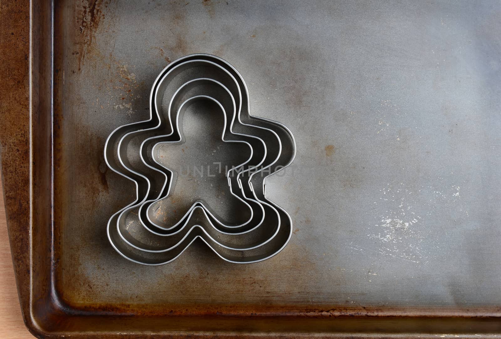 Overhead closeup of gingerbread men cookie cutters on a well used baking sheet. Horizontal format with copy space. Strong sidelight.
