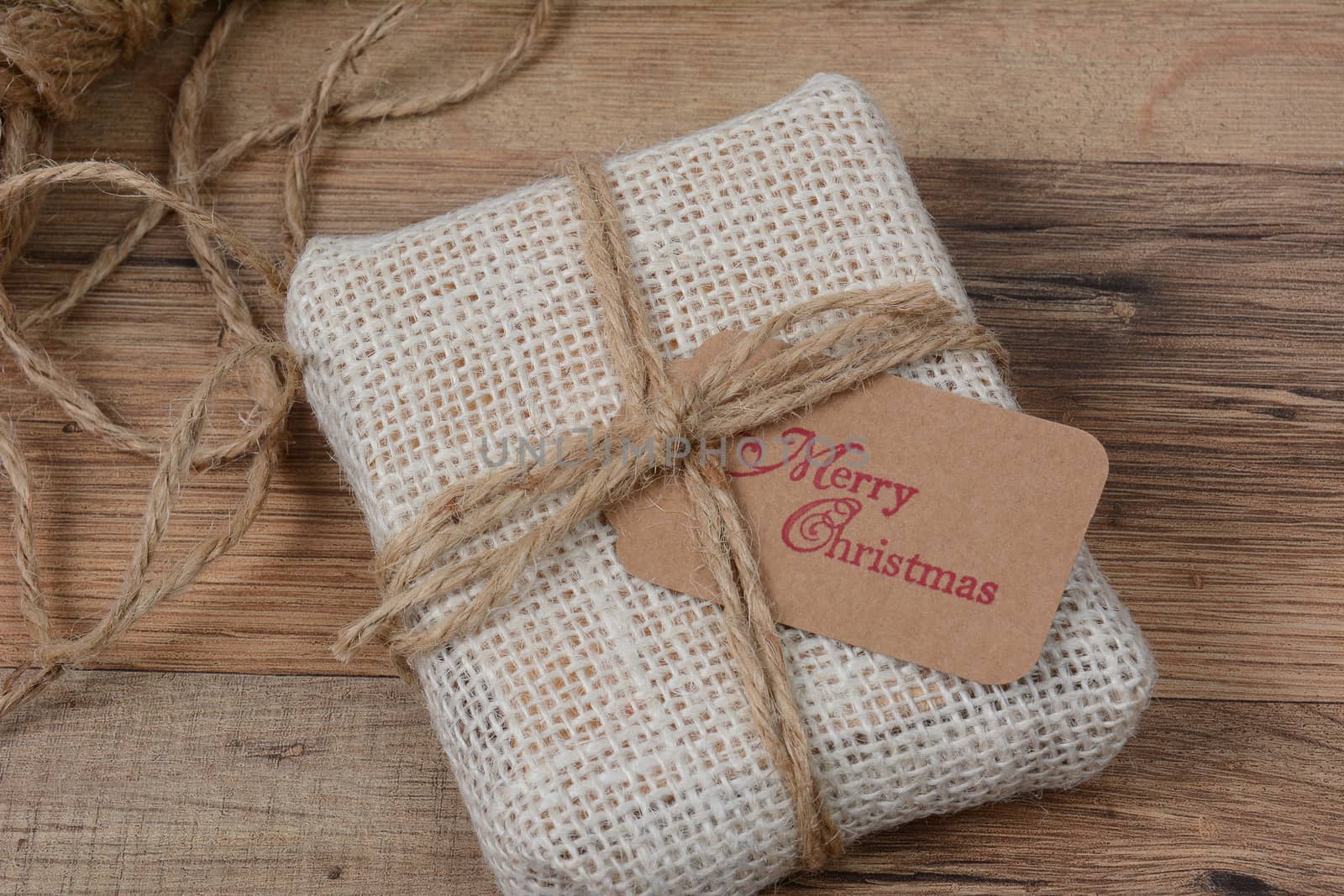 Closeup of a small fabric present with a Merry Christmas gift tag on a wood table.