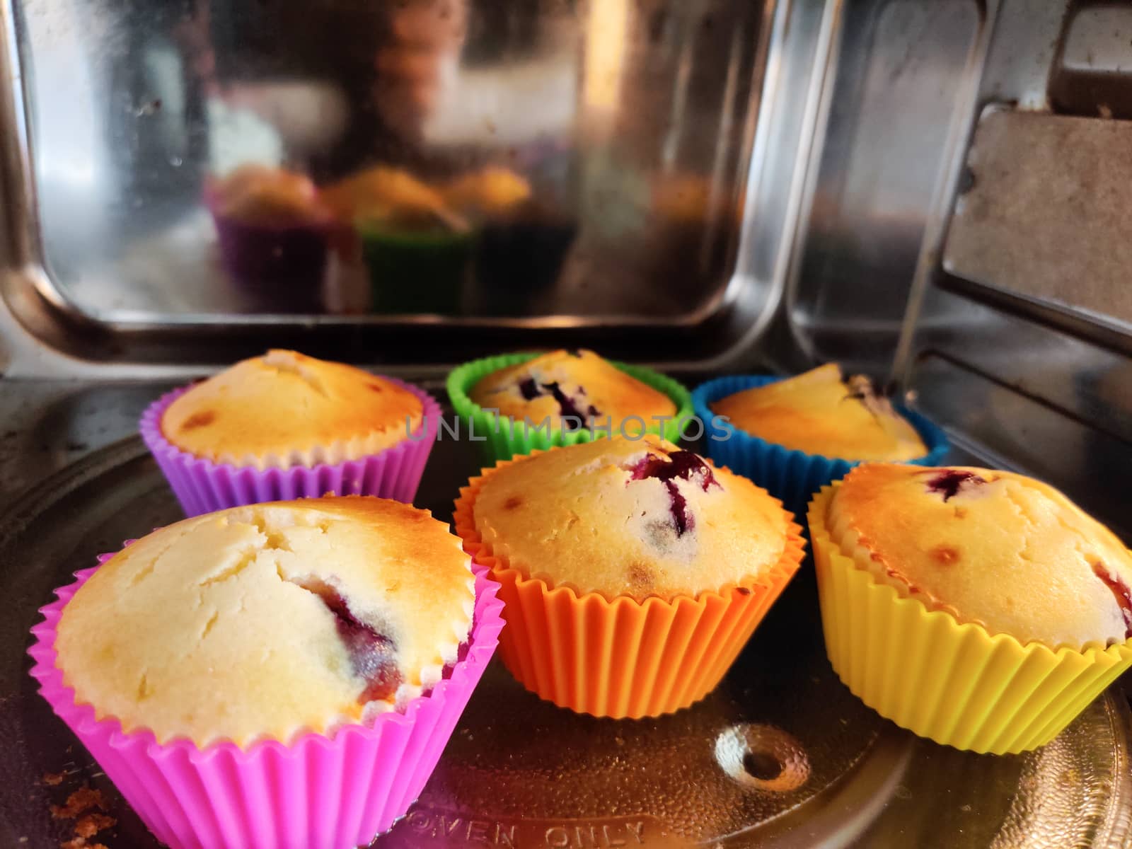 Freshly baked at home muffins in colorful cups placed in a shiny microwave. Shows the renewed interest in cooking due to the coronavirus pandemic lockdown