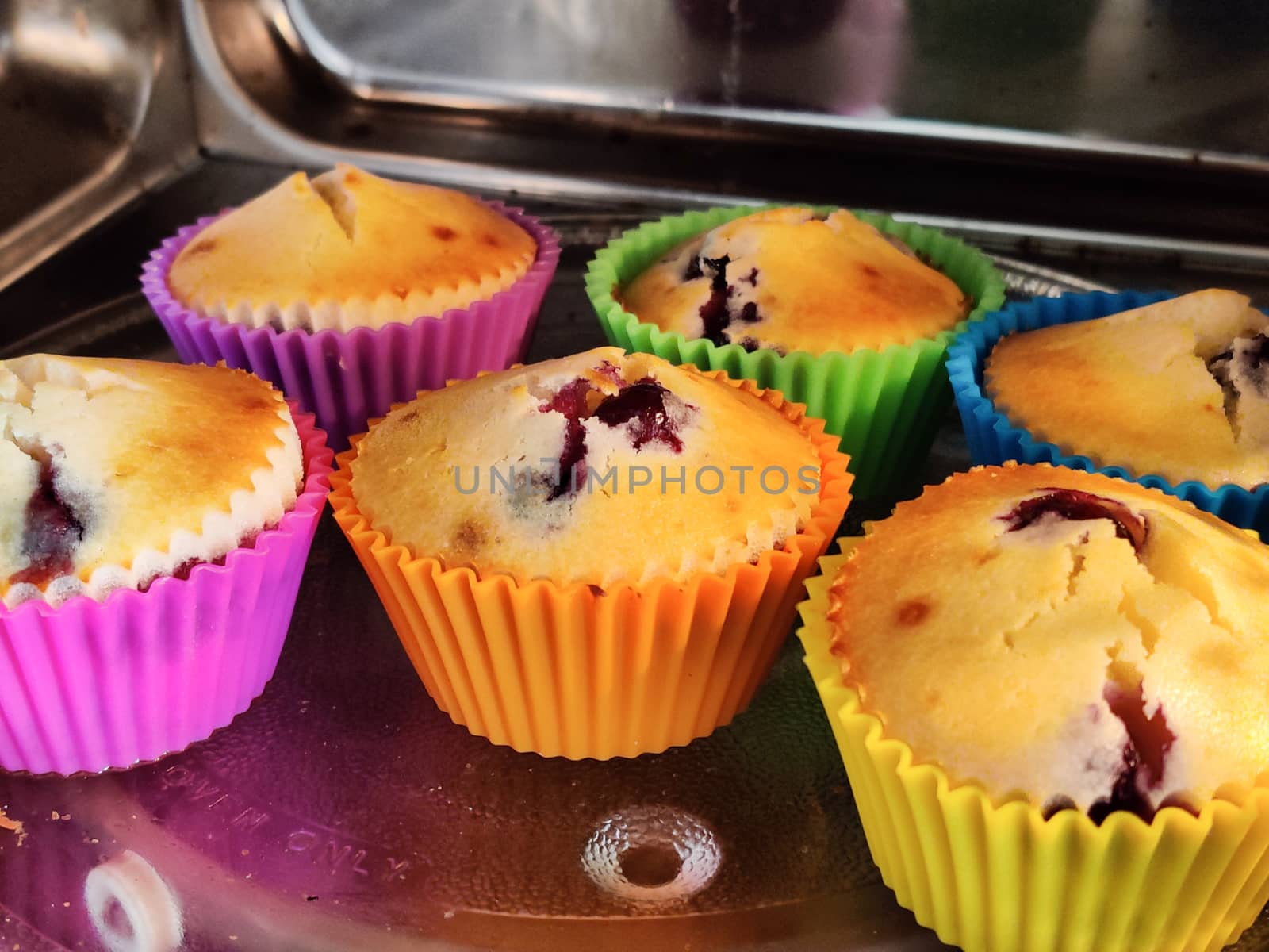 Freshly baked at home muffins in colorful cups placed in a shiny microwave by Shalinimathur