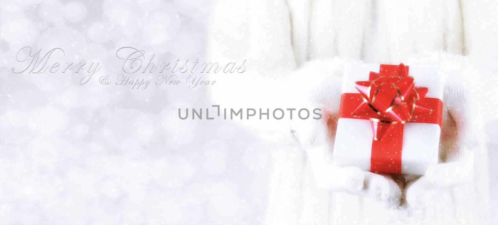 Closeup of a woman with a present in her hands with Merry Christmas and Happy New Year on a silver bokeh background and snow effect. Banner size with copy space.