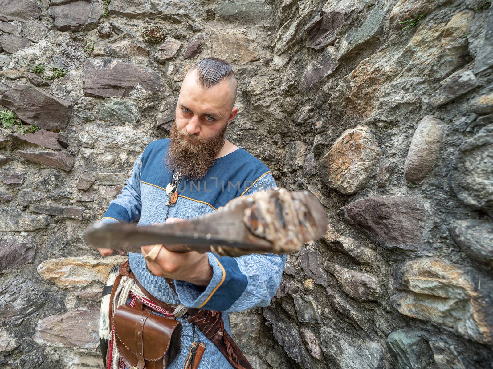 Portrait of a young Viking brandishing an ax in front of a stone wall, portrait set outdoors