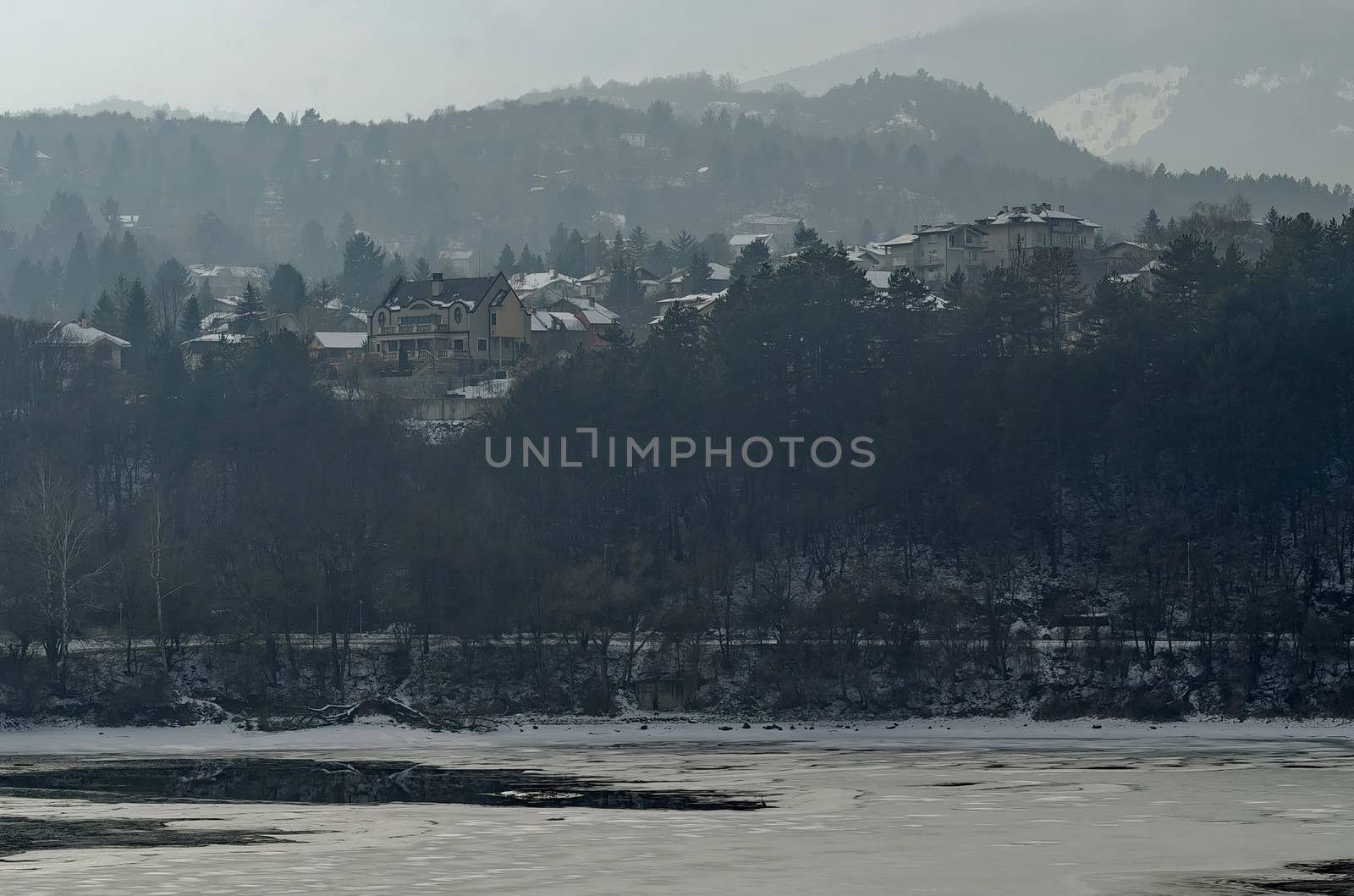 Winter scene with frozen lake, snowy mountain, glade, forest and residential district of bulgarian village Pancharevo, Sofia, Bulgaria