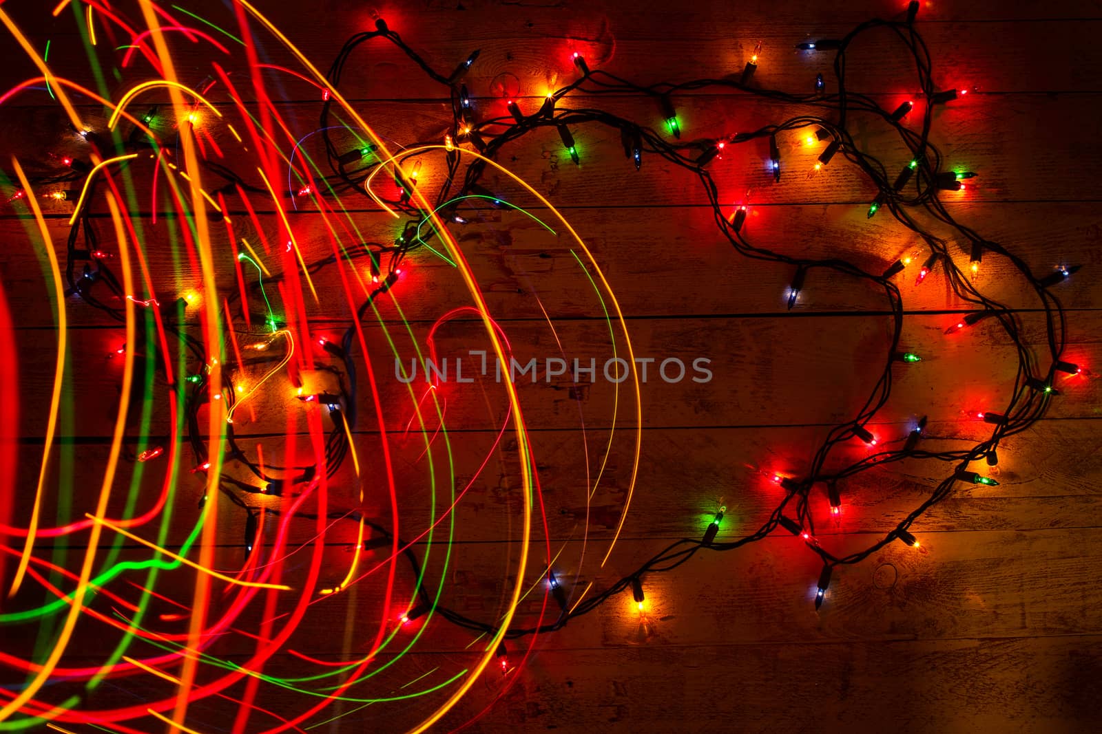 Colorful Christmas garland warm lights. Multicolored light lines. Wooden background. Long exposure. Top view. Horizontal shot. Copy space.