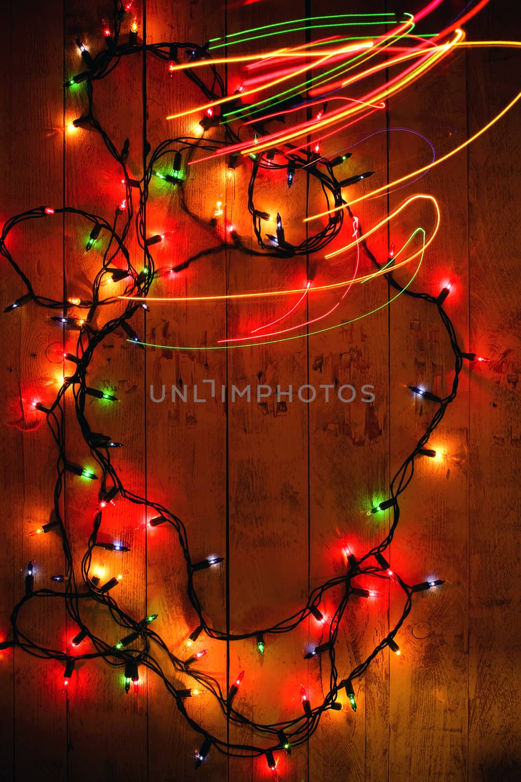 Colorful Christmas garland warm lights. Multicolored light lines. Wooden background. Long exposure. Top view. Vertical shot. Copy space.
