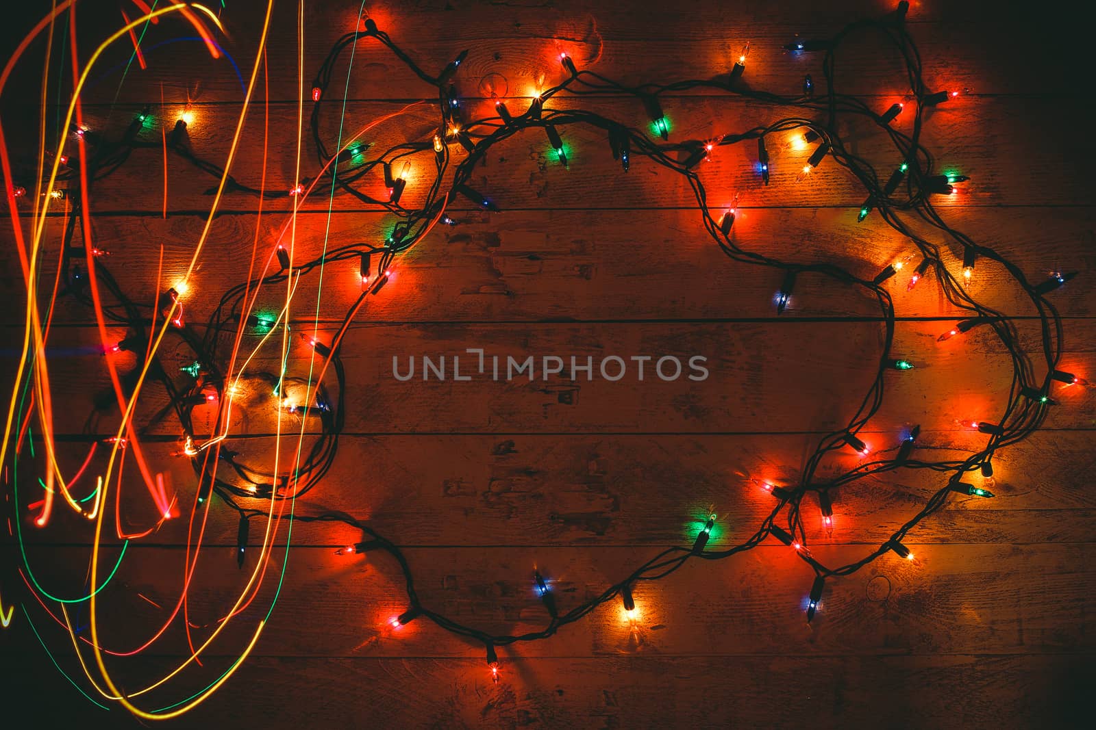 Colorful Christmas garland warm lights. Multicolored light lines. Wooden background. Long exposure. Top view. Horizontal shot. Copy space.