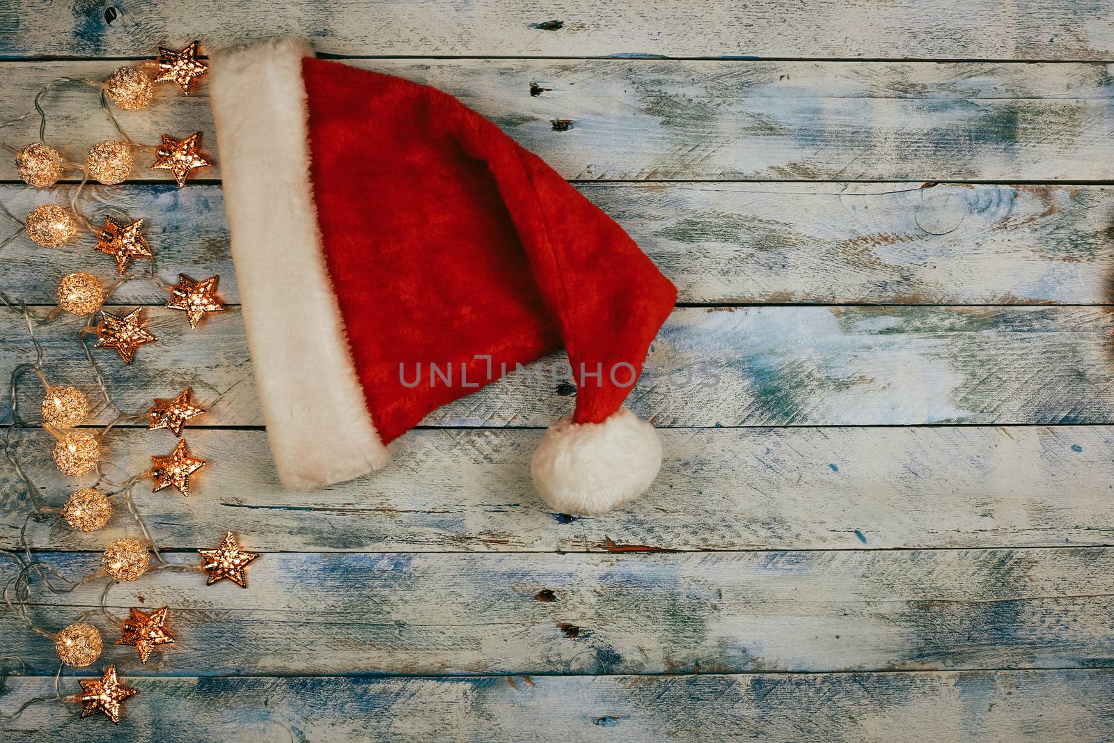 Christmas background with santa hat and christmas lights on rustic vintage wooden background. Garland. Flat lay, top view, copy space. Horizontal shot.