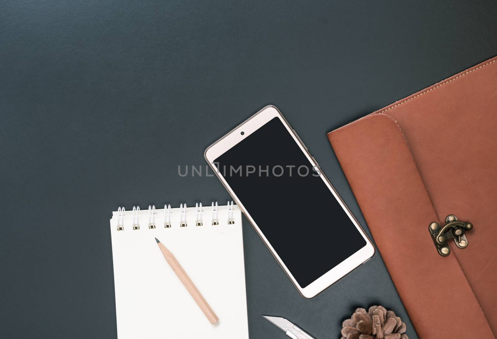 Workspace with mobile phone,leather bagnotebook,pen,pencil and stainless steel cutter on dark background,top view