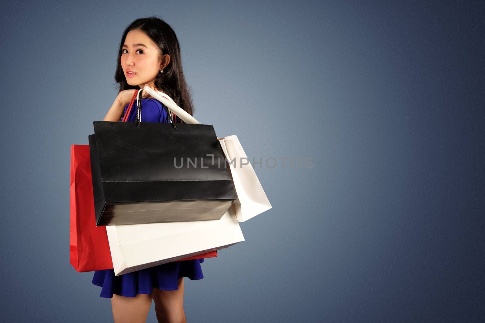 Happy women in blue dress with a shopping bag on dark blue background and clipping path with space for text