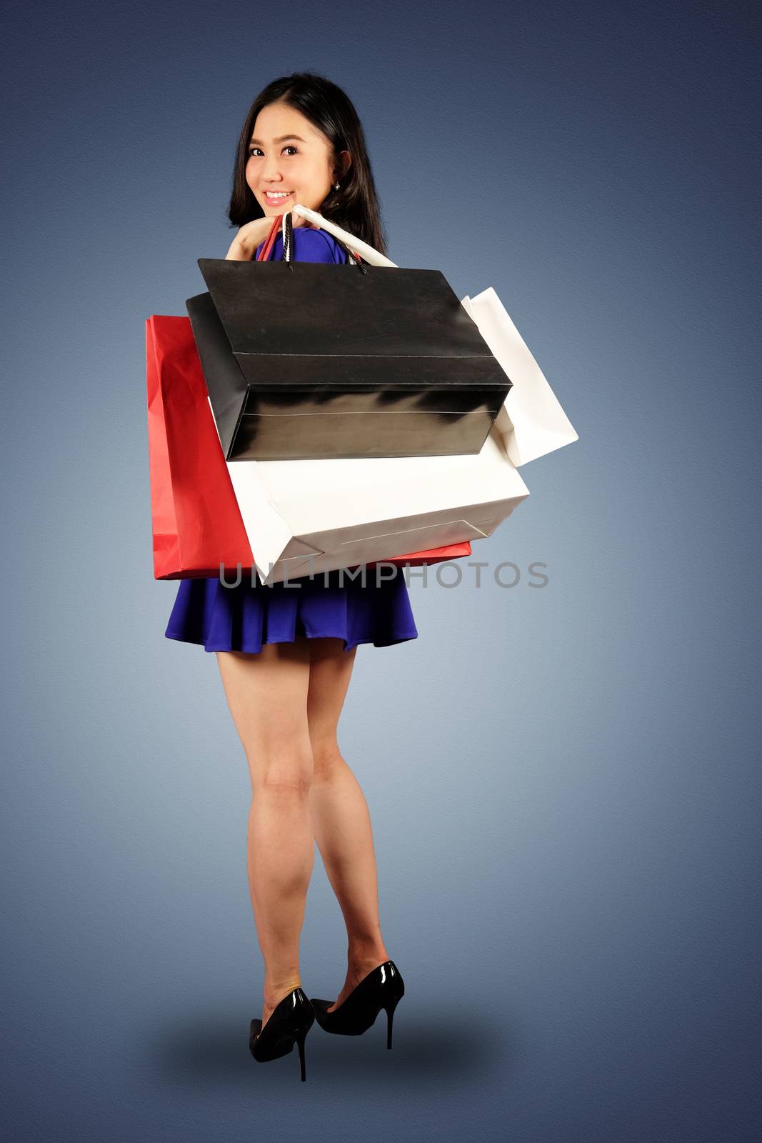 Happy women in blue dress with a shopping bag on dark blue background and clipping path