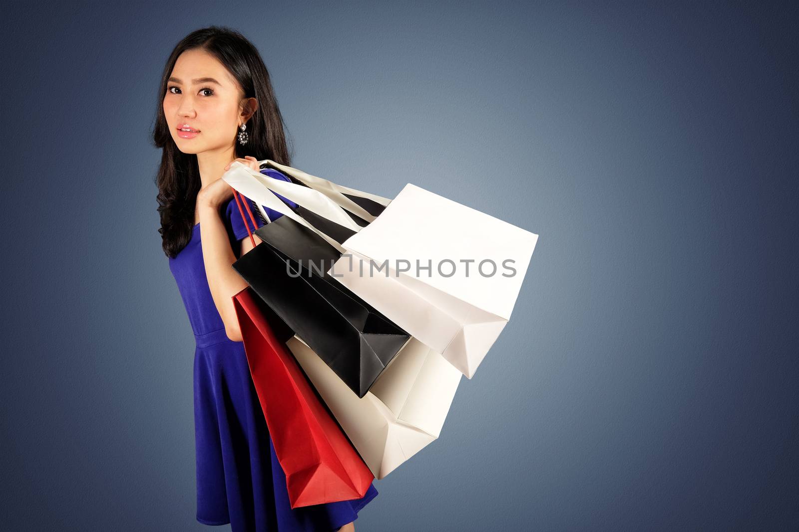 Happy women in blue dress with a shopping bag on dark blue background and clipping path