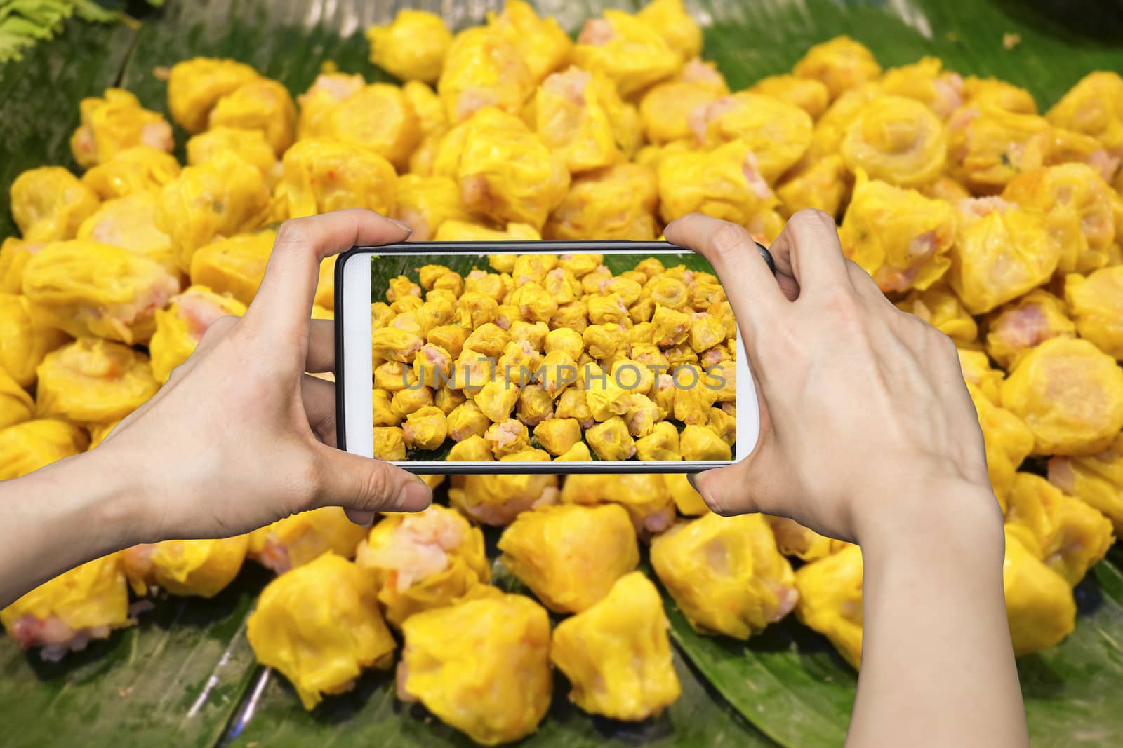 Girl taking pictures on mobile smart phone in Chinese Steamed Dumpling on banana leaf in Fresh maket