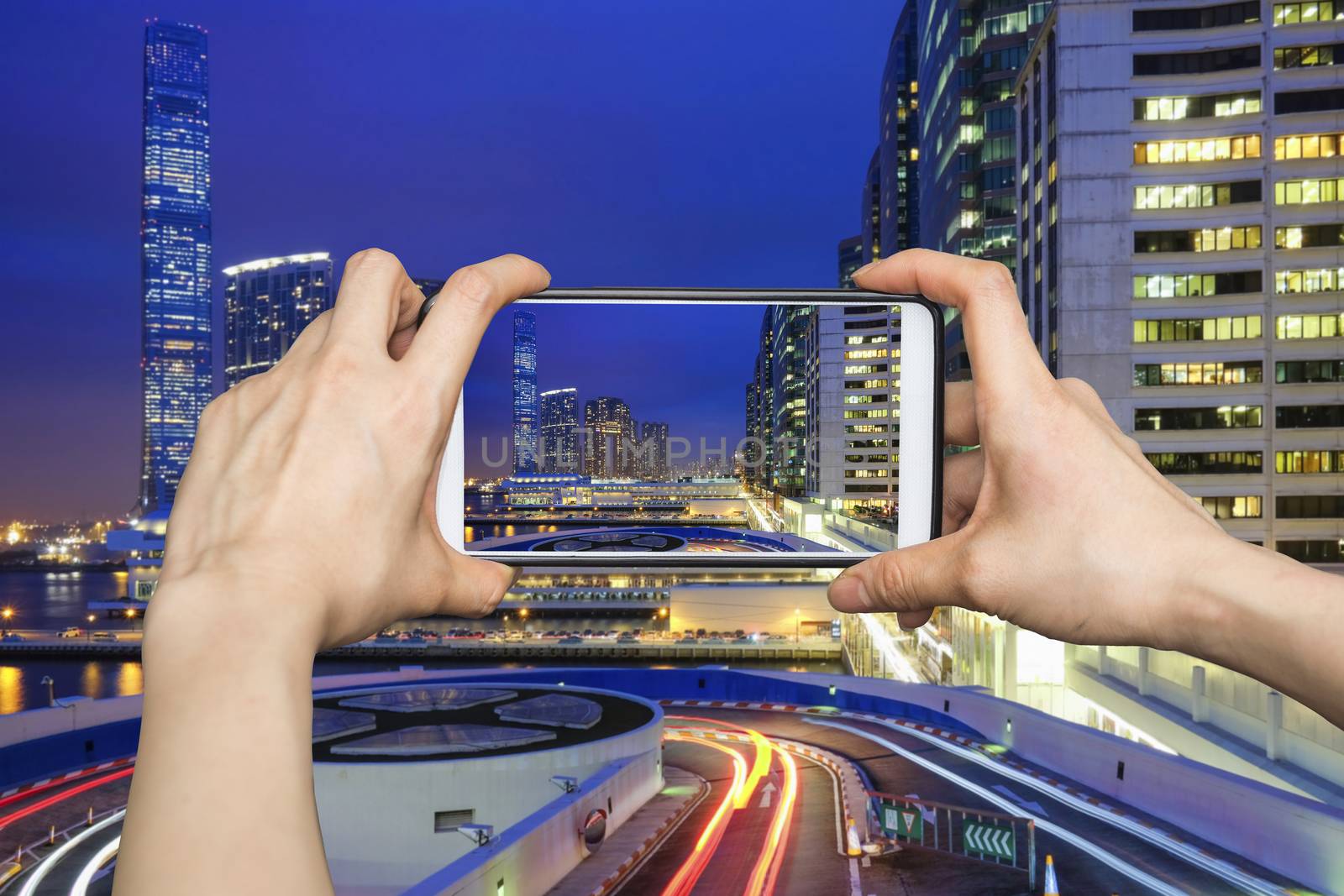 Girl taking pictures on mobile smart phone in Night view traffic in Hong Kong at sunset time
