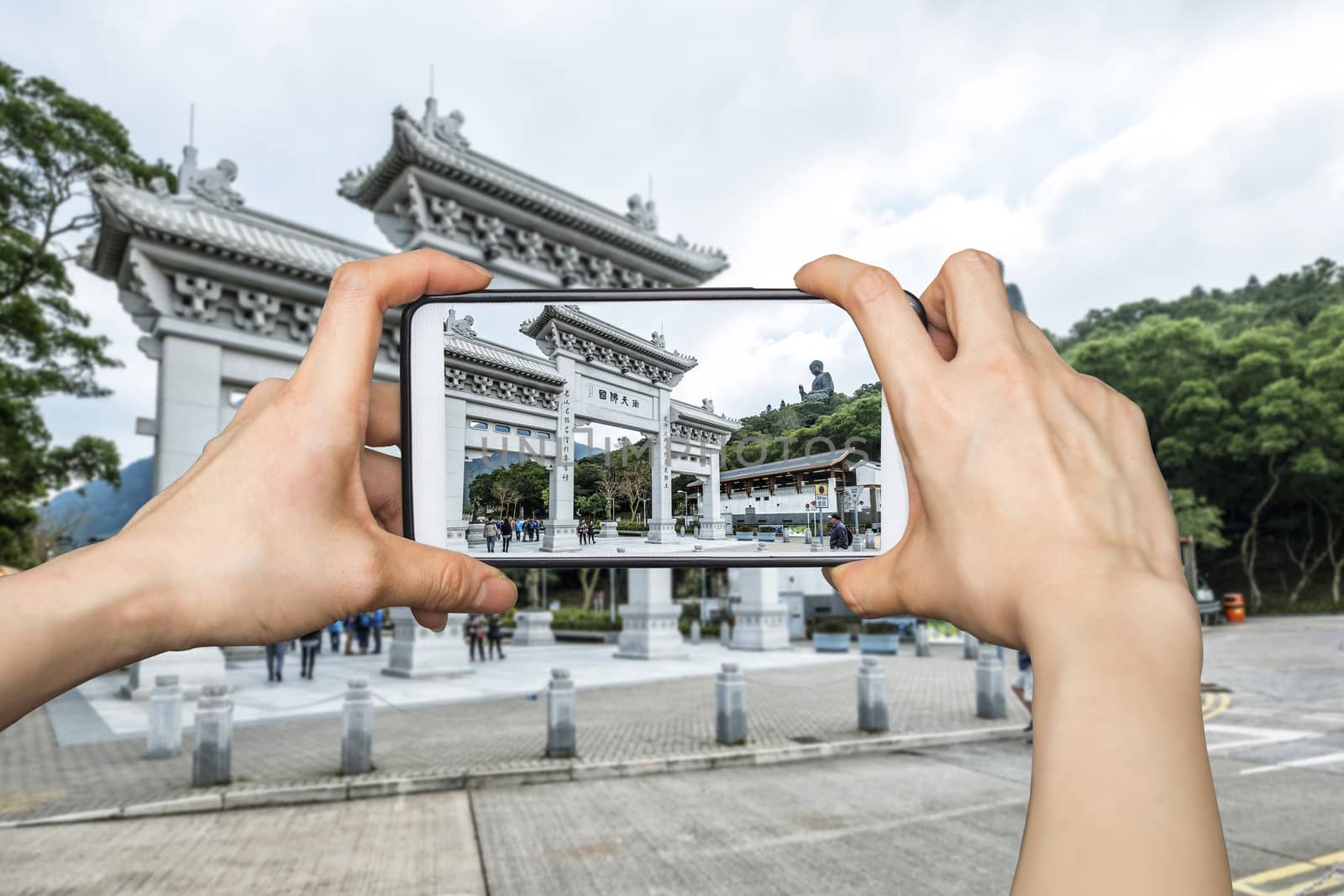 Girl taking pictures on mobile smart phone in Front View of Tian Tan Giant Buddha in blue sky