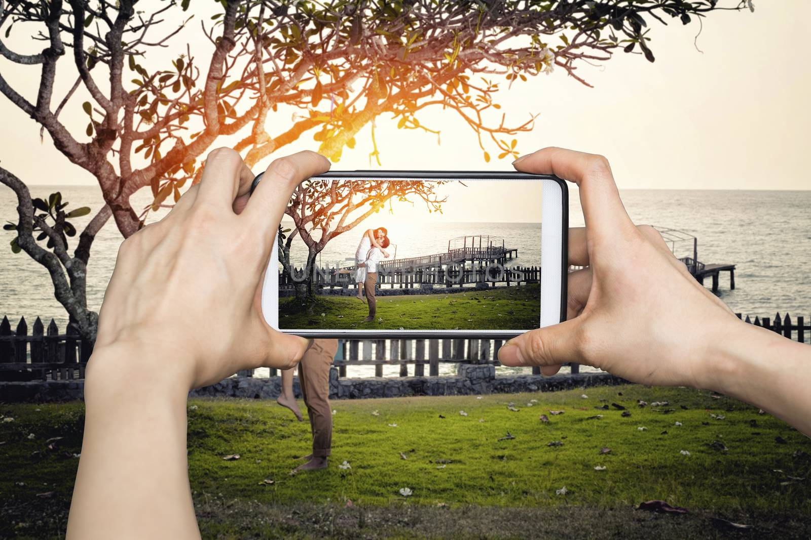 Girl taking pictures on mobile smart phone Happy couple relaxing in a tree by the sea